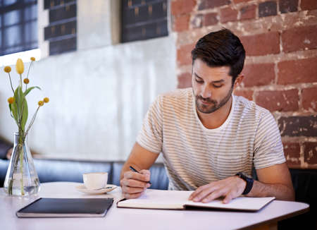 The write stuff. Shot of a handsome young man writing in a notebook while sitting at a restaurant...