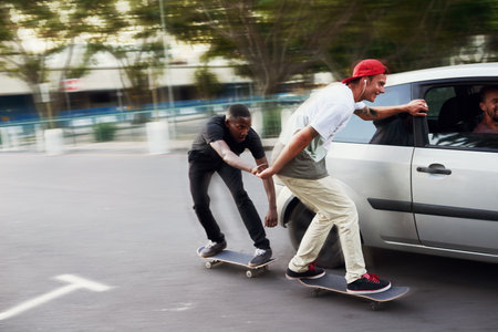 Never let your best friends do stupid things alone. Shot of two skaters holding on to a moving car.の写真素材