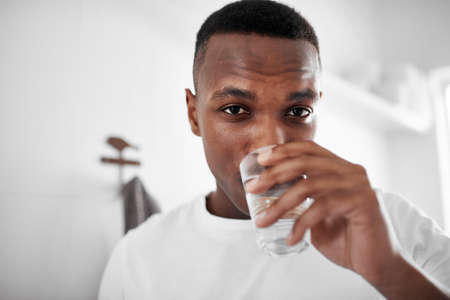 Drink water and stay healthy. Cropped shot of a young man drinking a glass of water at home.の写真素材