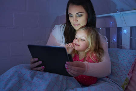 Five more minutes, please mom. Shot of a mother and daughter sitting in a bed reading a bedtime...