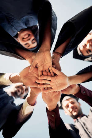 Theyve never felt more eager about the future. Closeup shot of a group of students joining their hands together on graduation day.の写真素材