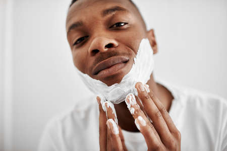 I prefer to shave it all. Cropped shot of a young man applying shaving foam to his face.の写真素材