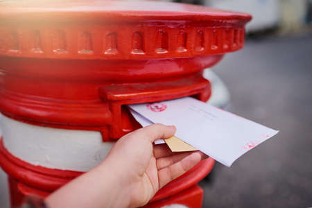 The old fashioned way of messaging. Closeup of an unrecognizable persons hand sliding in letters into a red mailbox outside during the day.の写真素材