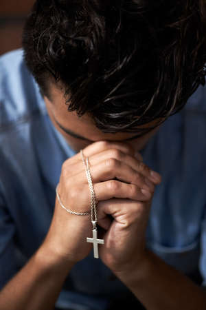 Praying for an answer. A young man bowing his head and holding a crucifix.の写真素材