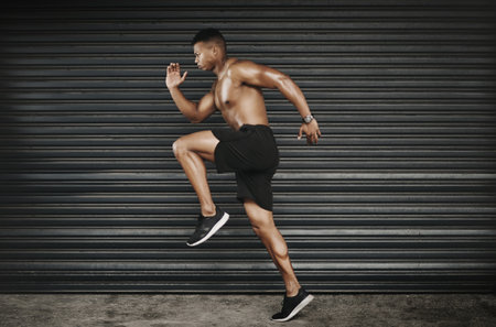 Feeling good and keeping fit. Shot of a fit and shirtless young man running.の写真素材