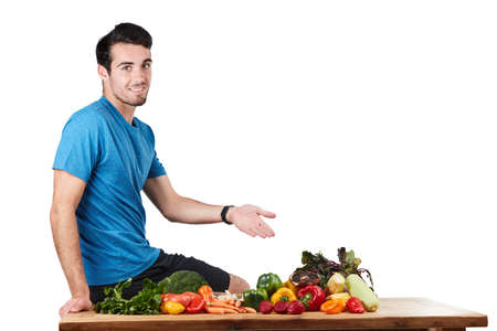 Fresh veg is on the menu today. Studio portrait of a handsome young man posing with a variety of fresh vegetables against a white background.の写真素材