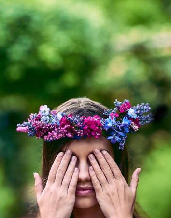 Dont cover your eyes, see the beauty around you. Cropped shot of a beautiful young woman wearing a floral head wreath and covering her eyes in nature.の写真素材