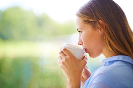 Contentment in a cup. Cropped shot of a young woman having coffee while standing by a window.