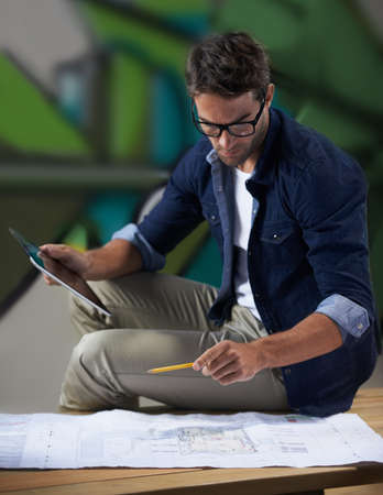 One final look at the plan before the presentation. Shot of a trendy male designer working on building plans at his desk.の写真素材