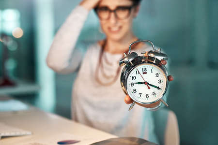 Theres just not enough time to complete those looming deadlines. Shot of a young businesswoman holding a clock worrying about her deadline at the office.の写真素材