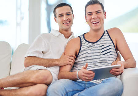 Everyday is special. Portrait of a gay couple using a digital tablet while relaxing on the sofa at...