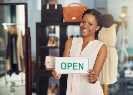 Ready to provide a top service to her customers. Portrait of a young business owner holding an open sign in her shop.の写真素材