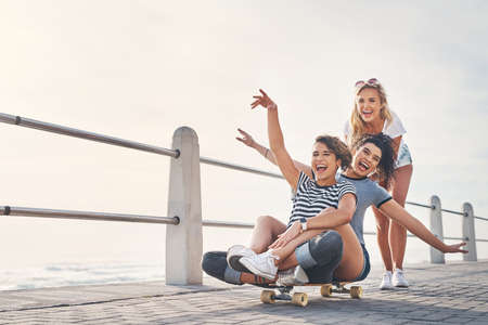 Were friends but more like sister. Shot of a woman pushing her friends on a skateboard while out on...