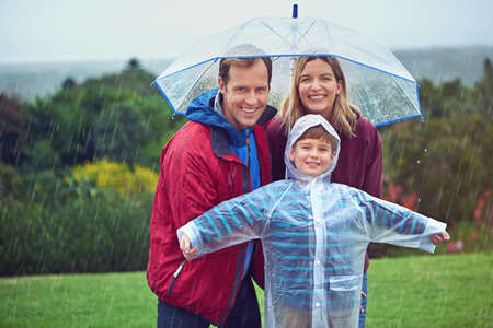 Its all smiles in the rain. Cropped portrait of a family of three standing outside in the rain.の写真素材