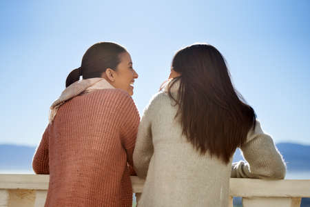 We share everything. Two young women standing outside on a balcony having a friendly conversation.の写真素材
