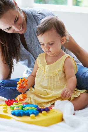 Teaching her little one. Shot of a cute baby girl sitting on the floor with her mom and playing with...