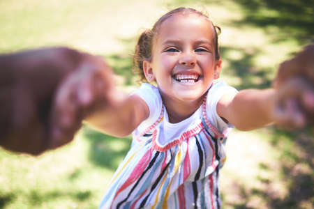 Swing me higher mom. Shot of a young girl being swung by her hands in the park.の写真素材