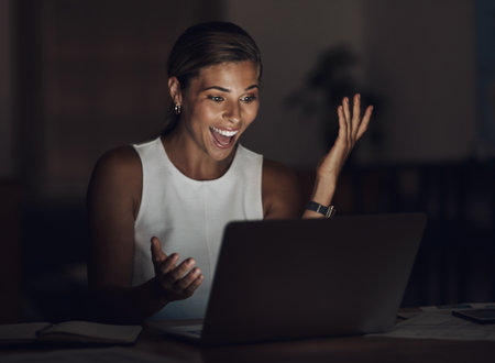 Her time was worth every dime. Shot of a young businesswoman using a laptop and looking surprised during a late night at work.の写真素材