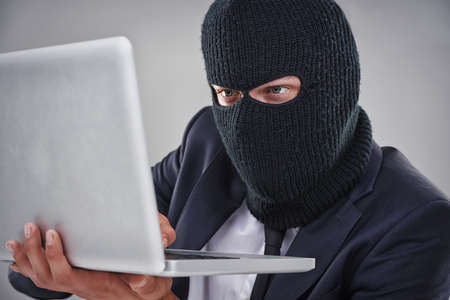 Hacking in to your secret files. Conceptual shot of a man with a mask over his head hacking in to a...