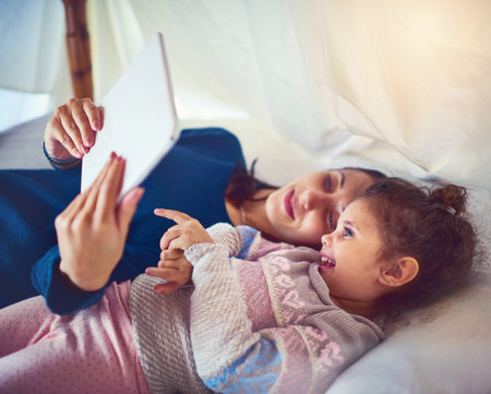 Interactive learning time. Shot of a mother and her little daughter using a digital tablet together at home.の写真素材