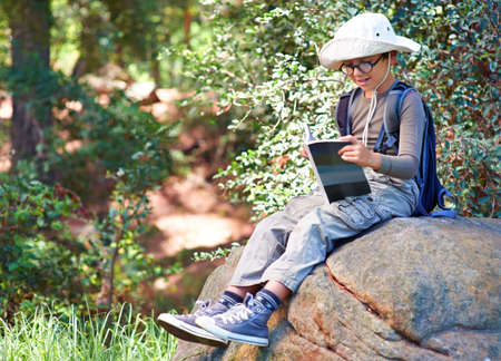 Reading up on owls. A little boy with a book in his hand sitting on a rock.の写真素材