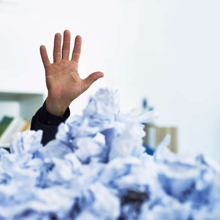 I could use a hand here. Shot of an office workers hand stacking out of crumpled up paperwork.の写真素材