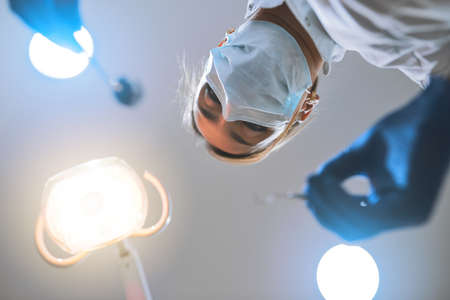 Just remain calm and Ill do the rest. Low angle shot of a focused young female dentist wearing a surgical mask while attempting to work on a patients teeth.の写真素材