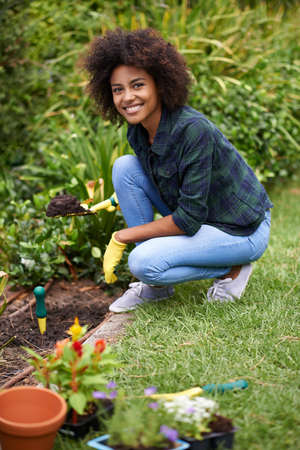 Getting her hands dirty. Portrait of a happy young woman planting flowers in the garden.の写真素材