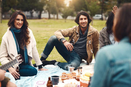Looks like were sorted with snacks. Shot of a group of cheerful young friends having a picnic together outside in a park during the day.の写真素材