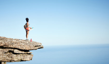 And then theres the big blue space.... Shot of a woman holding a map while standing on a mountain cliff.の写真素材