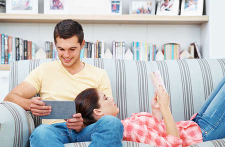 Reading together. A young couple relaxing at home on the sofa.の写真素材