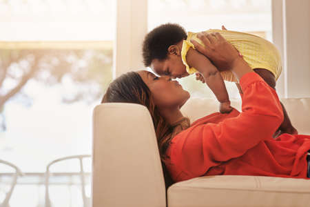 Youre my definition of perfect. Shot of a mother holding up her baby while lying on her sofa at...