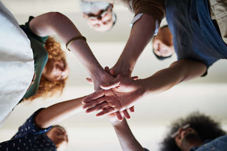 Lets get this project started. Low angle shot of a group of cheerful creative businesspeople forming a huddle with their hands inside of the office.の写真素材