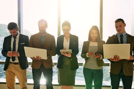 Working wireless. Cropped shot of a group of businesspeople using wireless devices while standing in...
