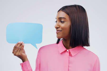 Im trying my best not to laugh. Shot of an attractive young woman holding speech bubble against a grey background.の写真素材