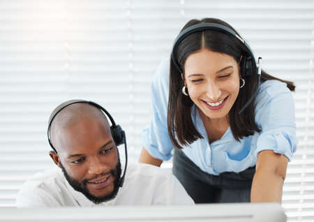 Need some help. Shot of a handsome young salesman sitting in the office and wearing a headset while...
