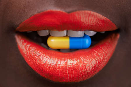 Taking a trip. Cropped view of an african woman with bright red lips with a capsule in her mouth.の写真素材