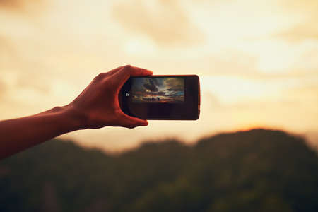 What a view. Closeup shot of an unidentifiable man taking a photo on his cellphone outside.の写真素材