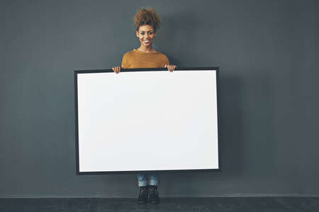 Ill advertise your message. Studio portrait of a young woman holding a blank sign against a grey...