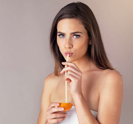 Sipping some vitamin c. Studio portrait of an attractive young woman drinking from an orange against a purple background.の写真素材
