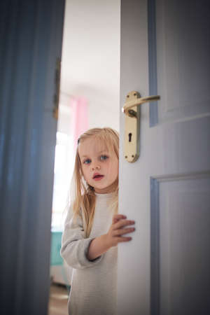 Knock knock, whos there. Shot of an adorable little girl opening a door at home.の写真素材