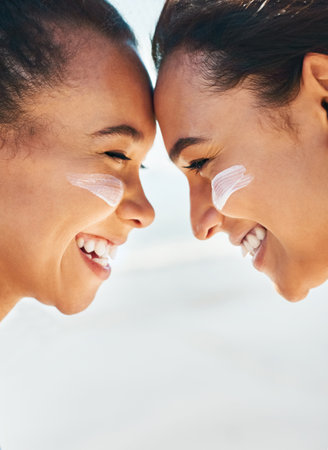 Sunscreen - Bring back the memories, not the burn. Shot of two beautiful young women at the beach with sunscreen on their faces smiling at each other.の写真素材