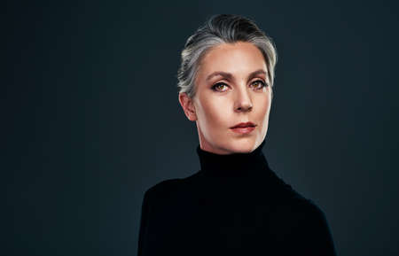 I aspire to be extremely sophisticated. Studio portrait of a beautiful mature woman posing against a dark background.の写真素材