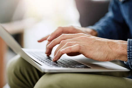 Deep into his passion.... Cropped shot of an unrecognizable man using a laptop in his living room at...