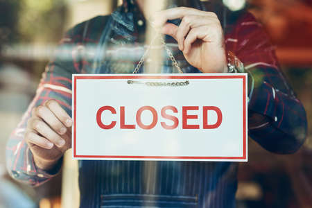 Closing up shop for the day. Closeup shot of a young man hanging up a closed sign in a shop window.の写真素材
