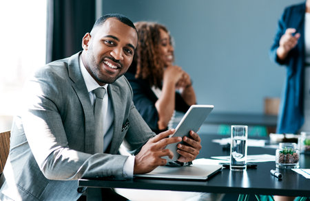 Theres always more to learn. Cropped portrait of a handsome young businessman working on his tablet during a meeting in the boardroom.の写真素材