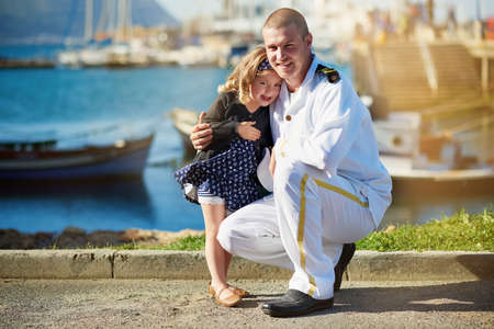 Dad and his darling. Portrait of a father in a navy uniform posing with his little girl on the dock.の写真素材