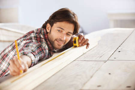 Perfect. A handsome young carpenter measuring and marking wood.