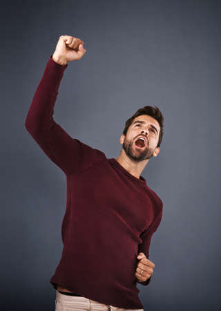 Now thats worth celebrating. Studio shot of a handsome young man cheering against a gray background.の写真素材