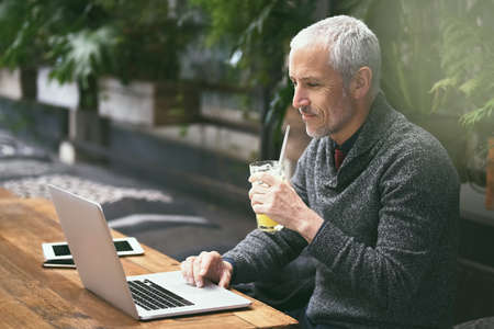 Its his favourite place to work. Shot of a mature businessman using his laptop in a cafe.の写真素材